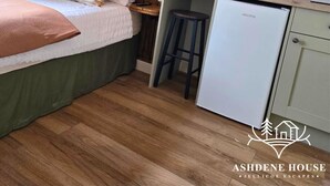 Een kleine slaapkamer met een bed, een bureau en een kitchenette.