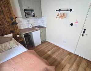 Een kleine kamer met een bed, een keukentje en een deur.