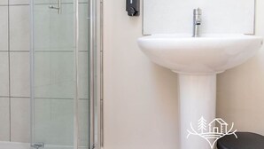 A bathroom with a glass shower enclosure, a white pedestal sink, and a wall-mounted soap dispenser. - Breeze Room 10 - Peaceful Single - New Forest (Dibden Purlieu)