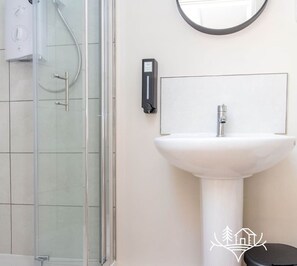 A bathroom with a glass shower enclosure, a white pedestal sink, and a wall-mounted soap dispenser. - Breeze Room 10 - Peaceful Single - New Forest (Dibden Purlieu)