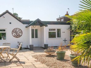 A white building with a circular logo on the wall, a patio with a table and chairs, and potted plants. - Breeze Room 10 - Peaceful Single - New Forest (Dibden Purlieu)