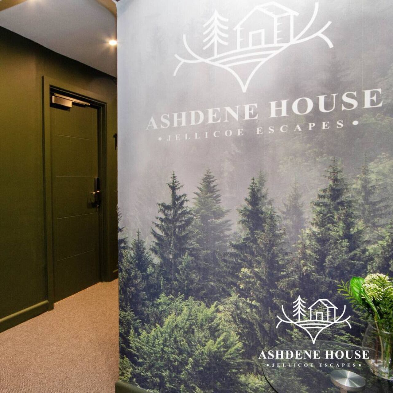 Un couloir avec une porte et une grande affiche représentant Ashdene House, avec une scène de forêt et le nom du domaine.