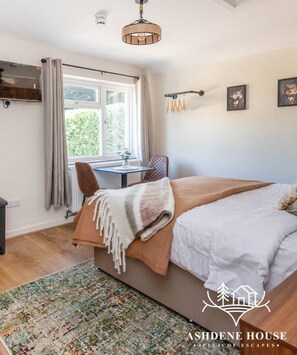 Une chambre à coucher avec un grand lit, un bureau, une chaise, une télévision et une fenêtre avec des rideaux.