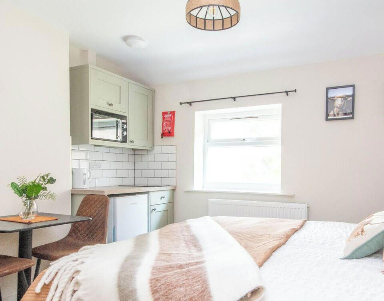 Une chambre avec un lit, une fenêtre, un coin cuisine et une table à manger avec des chaises.