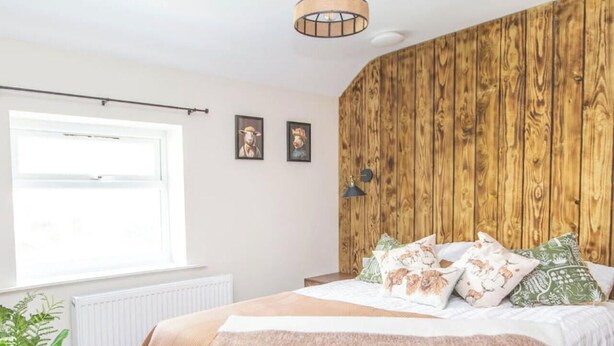 A bedroom with a wooden wall, a bed with patterned pillows, a bedside table with a glass, and a window. - Sheep Room 11 -Peaceful Double - New Forest (Dibden Purlieu)