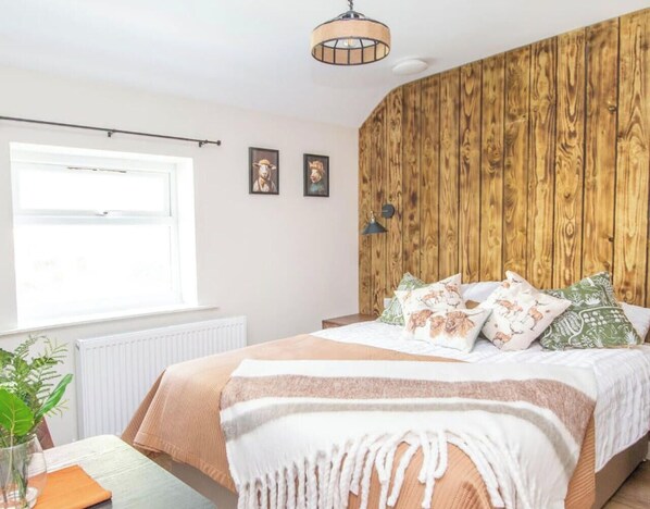 Een slaapkamer met een houten wand, een bed met opvallende kussens, een nachtkastje en een raam met zonwering.