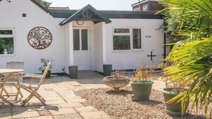 A white building with a circular logo on the wall, a patio with a table and chairs, and potted plants. - Sheep Room 11 -Peaceful Double - New Forest (Dibden Purlieu)