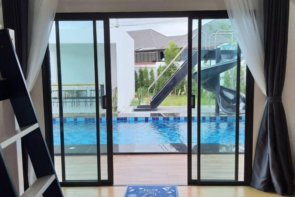 Vista a través de un ventanal corredizo a un área de piscina con una escalera y un tobogán.