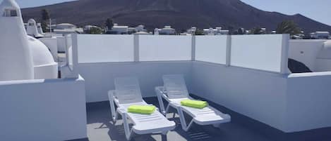 A rooftop terrace with two white lounge chairs and a mountain view.
