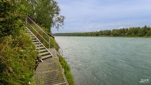 A metal staircase leading down to a river, surrounded by greenery and trees. - Kenai Riverside Escape (Soldotna)