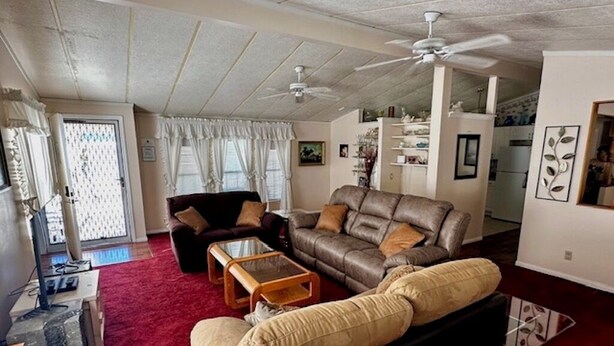 A living room with a brown leather sofa, a black sofa, and a red carpet. There is a ceiling fan, a coffee table, and a TV. - Retro Charm Meets Home Comfort- 2BR/2BA Rivered Desert Retreat with Boat Parking (Bullhead City)