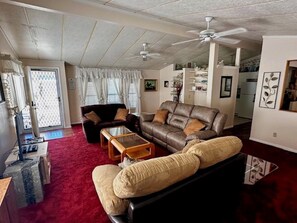 Un salon avec un canapé en cuir marron, un canapé noir et un tapis rouge. On y trouve un ventilateur de plafond, une table basse et un téléviseur.
