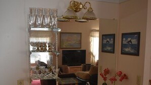 A kitchen with wooden cabinets, a sink, and a countertop. There is a mirror above the sink, and a shelf with glassware and a television in the background. - Retro Charm Meets Home Comfort- 2BR/2BA Rivered Desert Retreat with Boat Parking (Bullhead City)