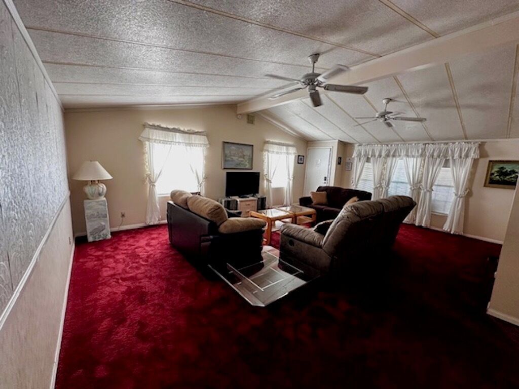 A spacious living room with a red carpet, two sofas, a coffee table, and ceiling fans.