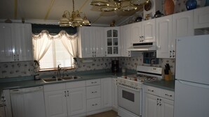 A kitchen with white cabinets, a stove, a sink, and a refrigerator. - Retro Charm Meets Home Comfort- 2BR/2BA Rivered Desert Retreat with Boat Parking (Bullhead City)