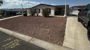 A parking lot with a gravel area, a building with a white facade, and a parked car. - Retro Charm Meets Home Comfort- 2BR/2BA Rivered Desert Retreat with Boat Parking (Bullhead City)