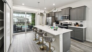 Una cocina moderna con una isla central, taburetes de bar y vistas a una piscina a través de puertas de vidrio.