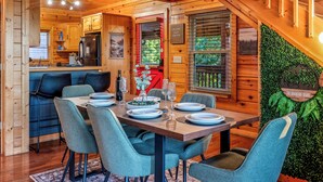 Interior de una cabaña de madera con comedor, cocina y una escalera.