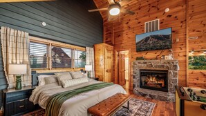 Un dormitorio acogedor con una cama grande, una chimenea de piedra y un televisor montado en la pared.