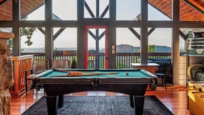 Una mesa de billar en una habitación con ventanas amplias y vistas al exterior.