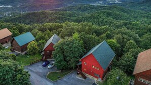 Un chalet à l’extérieur rouge, entouré d’une forêt dense, doté d’un vaste espace de stationnement et de plusieurs bâtiments.