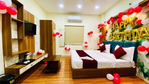 A hotel room with a bed, a TV, a minibar, and a wall decorated with balloons and a 'Happy Birthday' sign. - BELLA STAYS (Indore)