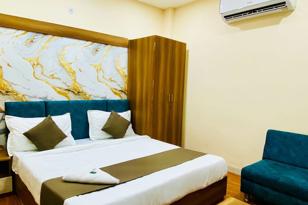 A hotel room with a bed, a wooden coffee table, a blue sofa, an air conditioning unit, and a marble-patterned wall.