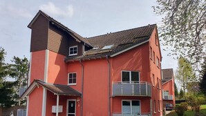 Un edificio de varios pisos con fachada roja, un balcón en el segundo piso y una pequeña entrada con puerta.