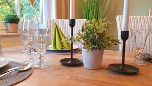 Una mesa de comedor dispuesta con cristalería transparente, una planta en maceta y una silla de mimbre.