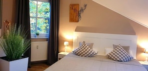A bedroom with a bed, two bedside tables, a window with curtains, a radiator, and a wall-mounted artwork. - Apartment 'Harzblick' with Private Terrace, Balcony and Wi-Fi (Braunlage)