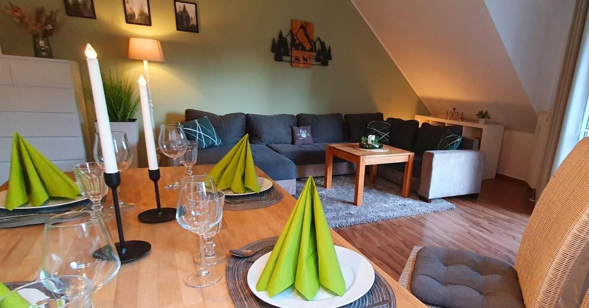 A dining area with a table set for a meal, a sofa, and a lamp in a room with a sloped ceiling.