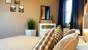 Un dormitorio con cama, cómoda, espejo, ventana con cortinas y decoración en la pared.