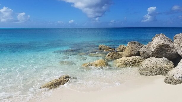Una playa con agua turquesa cristalina, arena blanca y rocas grandes.