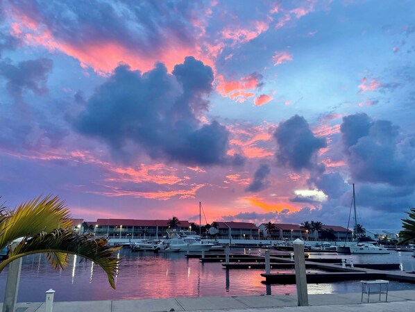 Un puerto deportivo con barcos amarrados, cielo despejado con nubes y edificios al fondo.