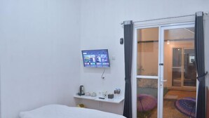 A bedroom with a bed, a TV mounted on the wall, a small shelf with items, and a sliding glass door leading to a balcony with umbrellas.