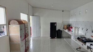 A room with a tiled floor, a refrigerator, a gas stove, and a shelf with various items.