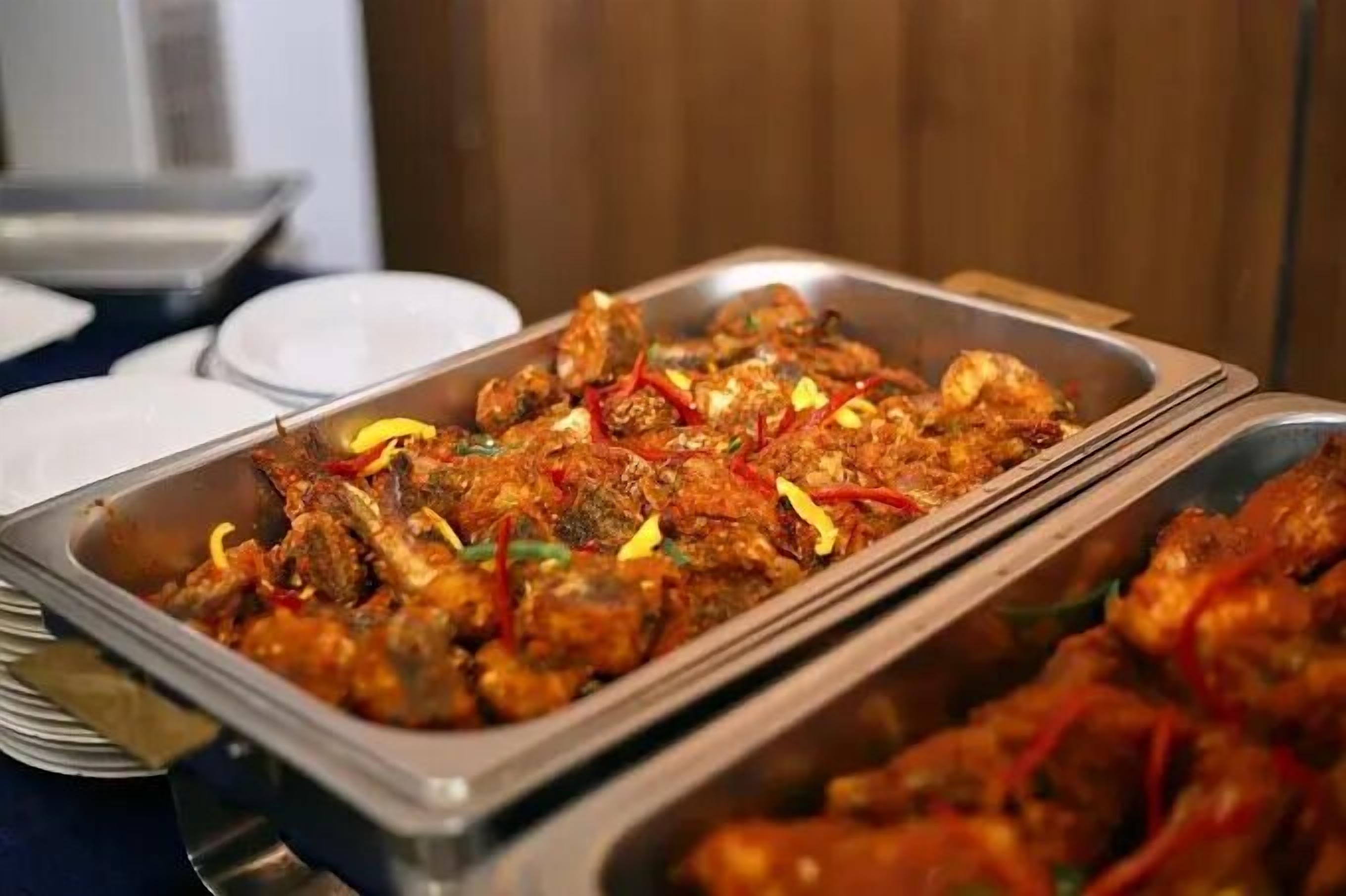 A buffet with various dishes, including what appears to be a meat dish garnished with red peppers and herbs.
