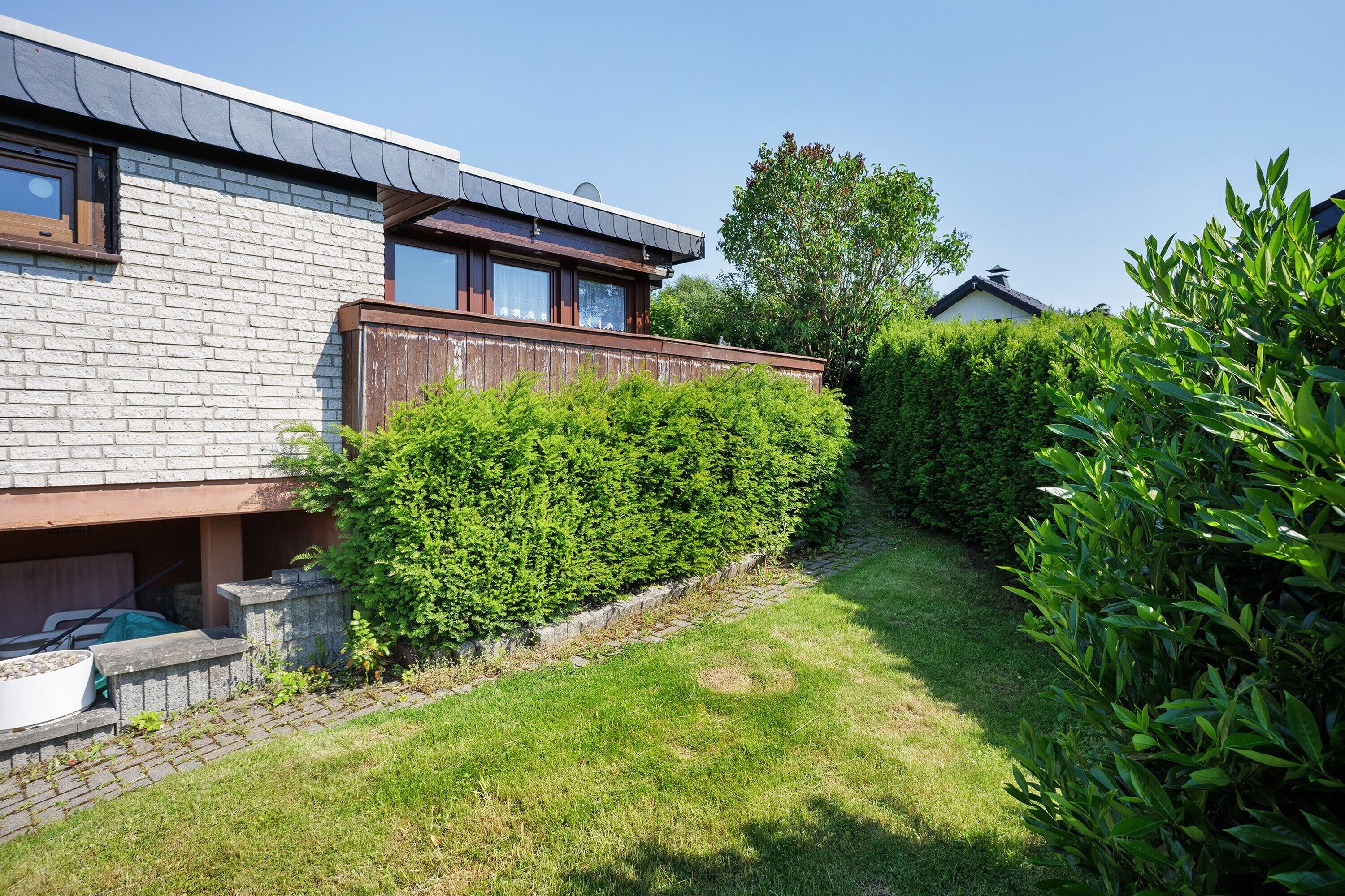 Una casa moderna con facciata in mattoni, un patio in legno e un giardino curato.