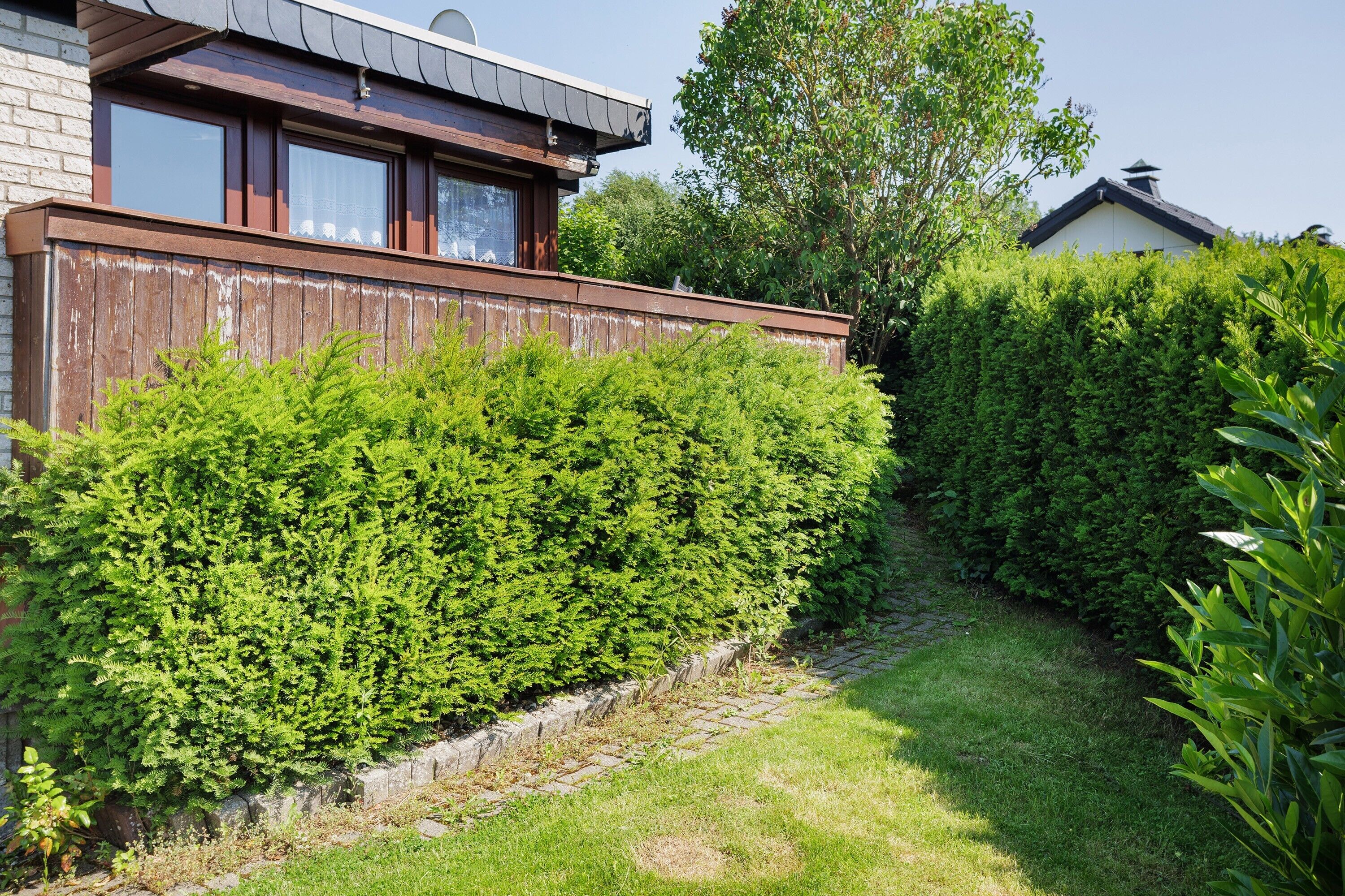 A modern house with a wooden fence, a well-maintained garden, and a clear sky.