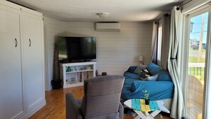 A living room with a television on a stand, a sofa, a chair, and a small table with a plant. - Coastal Charm in Caissie Cape Beach Community (Grande-Digue)