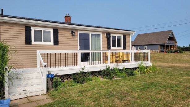 A two-story house with a white porch and a small deck. - Coastal Charm in Caissie Cape Beach Community (Grande-Digue)