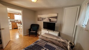 A bedroom with a bed, a TV, a chair, and a painting on the wall. - Coastal Charm in Caissie Cape Beach Community (Grande-Digue)