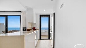 Eine moderne Küche mit Meerblick, ein Essbereich mit Tisch und Stühlen sowie eine kleine Kochinsel mit Spüle.