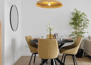 A dining area with a round table, four chairs, a hanging light fixture, and a potted plant.