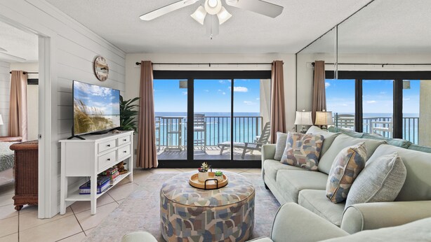 A living room with a television, a round coffee table, a sofa, and a balcony with a view of the sea.