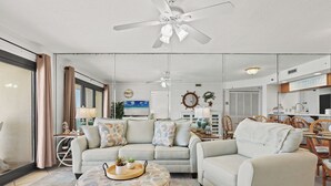 A living room with a sofa, armchair, ottoman, ceiling fan, and a dining area with chairs and a table.