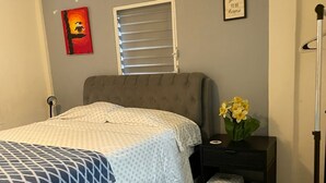 A bedroom with a bed, a nightstand, a window with blinds, a framed quote on the wall, and a painting. - Charming apartment with AC in Independence/Mango Creek. Near Placencia hot spot! (Independence and Mango Creek)