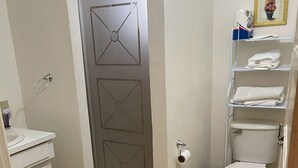 A bathroom with a toilet, sink, and a shower area. There are two yellow rugs on the floor. - Charming apartment with AC in Independence/Mango Creek. Near Placencia hot spot! (Independence and Mango Creek)
