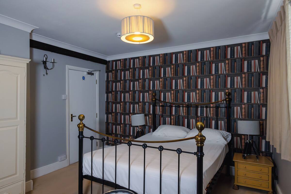 Un dormitorio con cama, lámparas de noche, una estantería y una puerta.