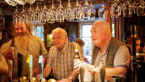A bar setting with multiple people, a variety of bottles, and a collection of wine glasses hanging from the ceiling. - The Rock Inn Hotel (Pub & Restaurant) (Taunton)